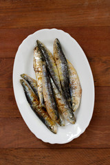 fried sardines on white dish on brown wooden background