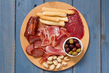 meat appetizer with olives and nuts on tray on blue wooden background