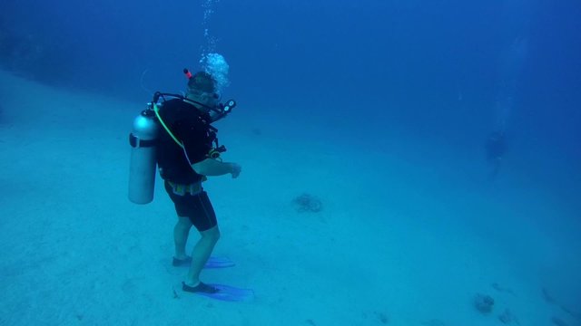 Diver standing on a sandy bottom in depth and awaits his buddy 