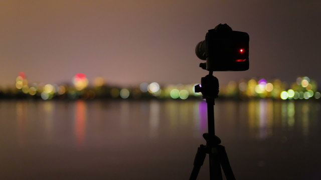 4 in 1 video! The camera and man with tripod stand by sunrise and lake with city bokeh night background