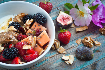 Bowl of home made fresh fruit muesli topped with strawberries,melon,blackberries,walnuts,chia seeds,peanut butter and walnuts. Served on a rustic wooden table with fresh wild flowers.