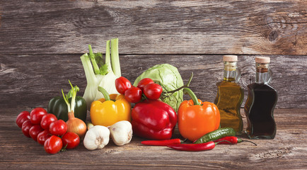 Colorful organic vegetables, olive oil, vinegar on wooden background 