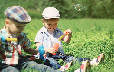 Two boys children sitting on the grass blowing soap bubbles, pla