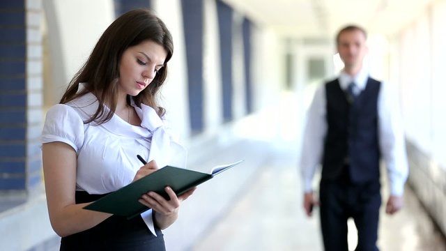 Business woman standing with a notebook, a businessman walking down the corridor