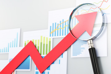 Looking upside growth arrow with magnifying glass. Graphs and da