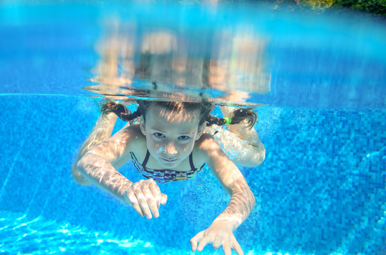 Happy girl swims in pool underwater, active kid swimming, playing and having fun