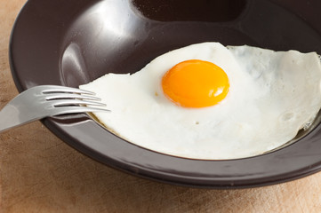 view of a fried egg served on dark dish with fork