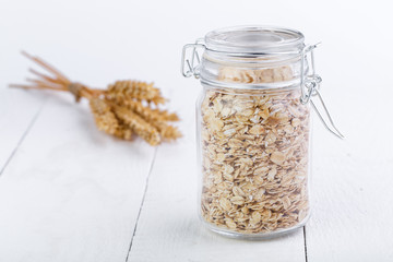 The oat flakes in glass jar and wheat.