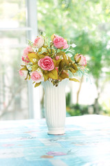 artificial roses in ceramic vase near window with morning light, in soft blue color