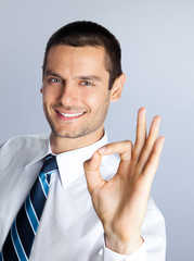 Smiling businessman showing okay gesture, against grey