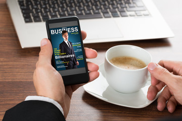 Businessman Looking At Magazine On Cellphone