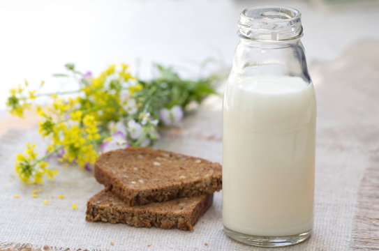 Bottle of milk, rye bread and summer flowers