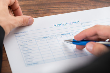Person's Hand Filling Blank Weekly Time Sheet