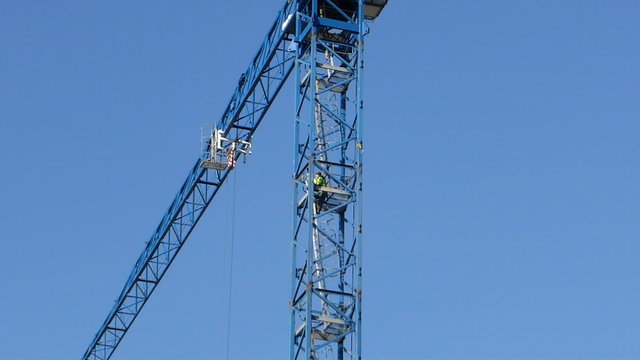 Worker climbing the ladder of working construction crane