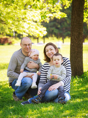 Portrait of mother, father, daughter and son, happy family of four, sitting on the meadow in the park outside on a spring summer bright day