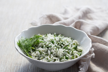 Rice with greens in a white bowl on a wooden table