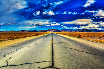 Tar lines of an open, desert highway as clouds dance on the horizon near Death Valley, California