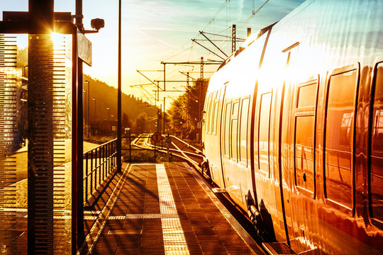 Fototapeta Modern passenger train standing at countryside platform with beautiful landscape at sunset.