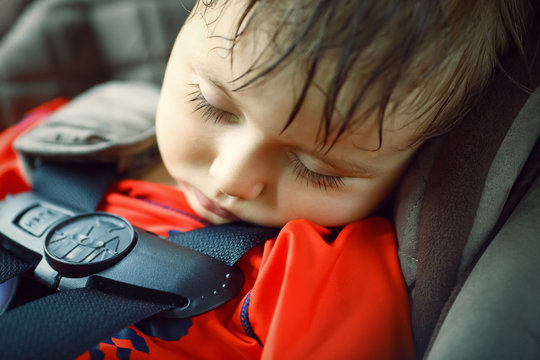Closeup portrait of a cute adorable little boy toddler tired and sleeping belted in car seat on his trip, safety protection concept