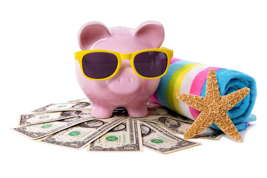 Piggy Bank or piggybank wearing sunglasses standing on pile heap of US American dollar bills with beach towel holiday vacation retirement saving money plan photo isolated white background