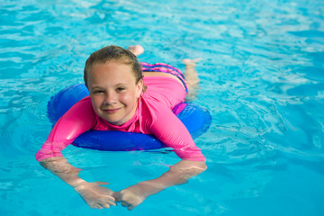 Smiling little girl in swimming goggles relaxing in the swimming pool