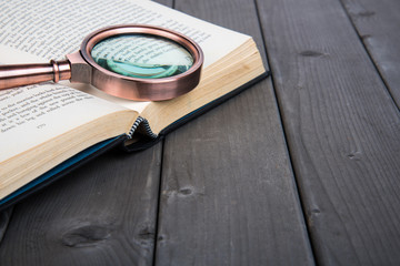 Vintage books and magnifying glass on wooden background
