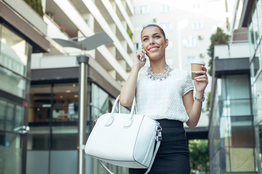 Young businesswoman holding coffee to go and talking on the phon