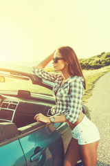 Attractive young woman posing leaning on convertible car 