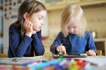 Two children playing with a digital tablet at home - obrazy, fototapety, plakaty