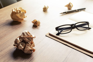 Crumpled paper balls with eye glasses and notebook on wood desk