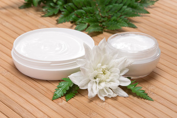 Obraz na płótnie Canvas Jars of cream with white flower and fern leaves