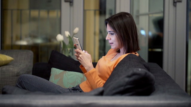 Young woman using smartphone lying on sofa at home
