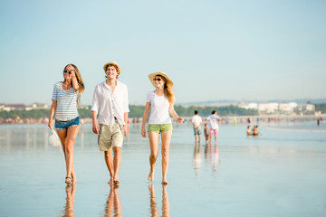 Group of happy young people walking along the beach on beautiful