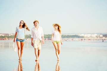 Group of happy young people walking along the beach on beautiful