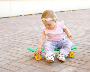 Cute baby sitting on the skateboard outdoors in city