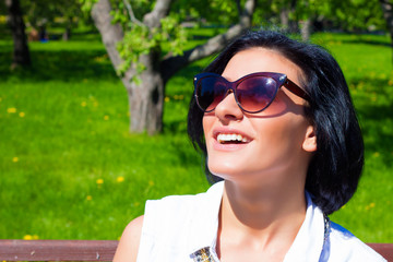 Attractive brunette in sunglasses laughing in the park on a sunny day