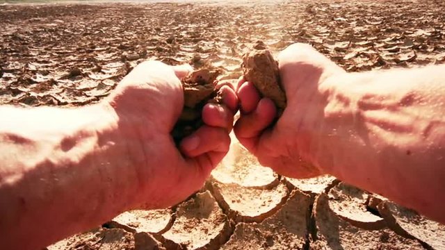 Farmer's hands split piece of dry soil from field affected by drought. Slow-mo