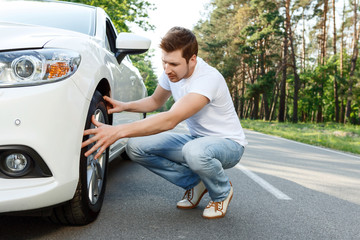 Young man checking tire of his car