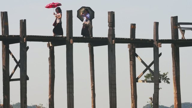 Burmese women walk on wooden bridge. U Bein bridge is longest teak bridge