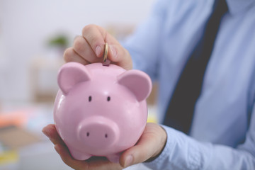 Businessman putting coin into small piggy bank