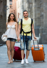 Fototapeta na wymiar couple in shorts with luggage walking through city
