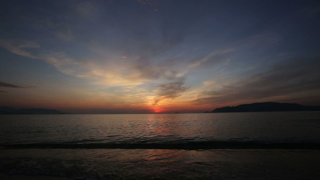 panorama of sun rising from behind horizon through fantastic clouds above sea