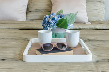 glasses on black book with cup of coffee in wooden tray and vase