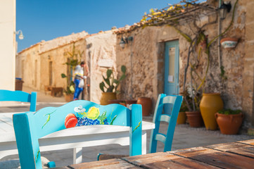 Painted wooden chair in the main small square of the fishing village Marzamemi, Sicily, and some typical stone houses in the background