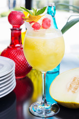refreshing glass of bright juicy melon smoothie or lemonade with ice on a table at a restaurant with the decor of the bright dishes and pieces of melon