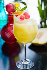 refreshing glass of bright juicy melon smoothie or lemonade with ice on a table at a restaurant with the decor of the bright dishes and pieces of melon