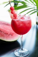 refreshing glass of bright juicy watermelon smoothie or lemonade with ice on a table at a restaurant with the decor of the bright dishes and pieces of watermelon