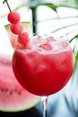 refreshing glass of bright juicy watermelon smoothie or lemonade with ice on a table at a restaurant with the decor of the bright dishes and pieces of watermelon