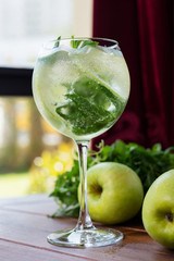 refreshing glass of cold apple lemonade with mint and ice on a wooden table in a restaurant with a creative decoration of mint leaves and fresh apples. soft focus