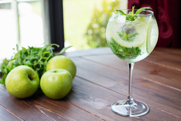 refreshing glass of cold apple lemonade with mint and ice on a wooden table in a restaurant with a creative decoration of mint leaves and fresh apples. soft focus